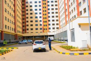 a man standing next to a white car in a parking lot at Fp&b apartments in Kisumu