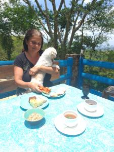 a woman holding a dog at a table with food at Hotel Fazenda Casa Mato in Taubaté
