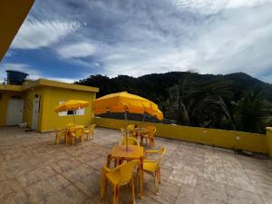 een patio met tafels en stoelen met gele parasols bij Recanto Guaraú 4 in Peruíbe +9 foto's