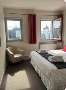 a bedroom with two beds and a chair and two windows at 2 bedrooms in the sky ! in Neuilly-sur-Seine +13 photos