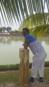 Un hombre apoyado en un poste de madera cerca de un cuerpo de agua. en Suite Property Insurance Group Of Company, en Dhaka