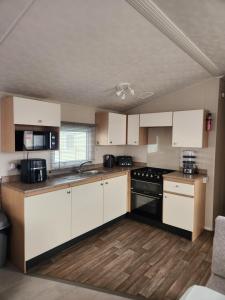 a kitchen with white cabinets and black appliances at Sam's Caravan Hire in Ingoldmells