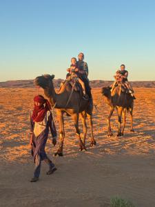 a group of people riding on the backs of camels in the desert at Bivouac La Dune Blanche in Mhamid