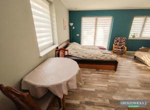 a bedroom with a bed and a table and two windows at Przytulne i ciepłe mieszkanie w spokojnej dzielnicy Opola in Opole