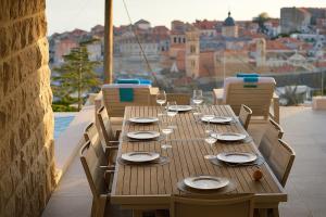 a wooden table with chairs and plates and wine glasses at Villa D' Republic Dubrovnik - Infinity Pool & Old Town Views in Dubrovnik +62 photos