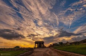 a cloudy sky with a monument in a field at Gopi Abode Hampi in Hampi