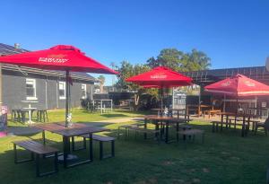un grupo de mesas de picnic con sombrillas rojas en Royal Mail Hotel Mulwala, en Mulwala