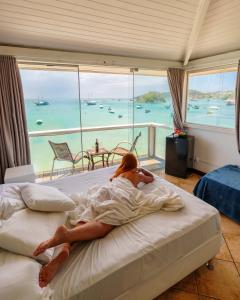 a woman laying on a bed with a view of the ocean at Bamboo Búzios Hostel in Búzios