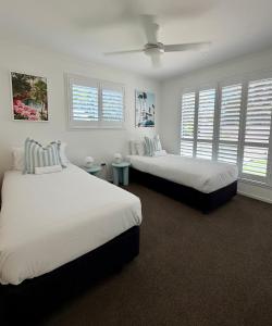 two beds in a room with white walls and windows at The Little Tropicana in Byron Bay