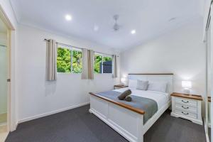 a white bedroom with a bed and two windows at Tropical Resort Apartment in Cannonvale