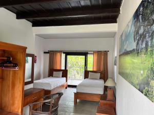 ein Schlafzimmer mit zwei Betten und einem Schreibtisch und einem Fenster in der Unterkunft Dhita Dive Bungalow in Ambat