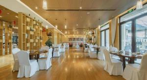 un restaurant avec des chaises et des tables blanches dans une salle dans l'établissement Deefly Yinrun Town Hotel, à Deqing