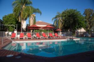 a swimming pool with red chairs and umbrellas at Airtel Plaza Hotel in Van Nuys