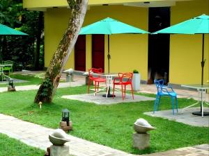 une table avec des chaises colorées et des parasols dans une cour dans l'établissement Bridge Hotel Negombo, à Dagonna