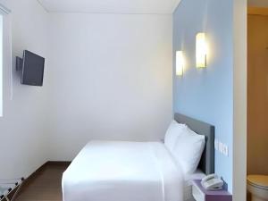 a bedroom with a white bed and a phone at Amaris Hotel Palangkaraya in Palangkaraya