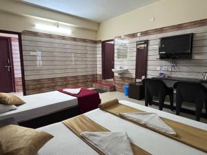 Habitación con 2 camas, mesa y TV. en Yammuna Vihaar Tourist Home, en Kollūru