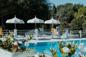 a pool with white umbrellas and tables and chairs at Green Garden Village in Sirolo