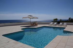 a swimming pool with an umbrella and chairs and the ocean at Villa Es Gallinots in Mahón