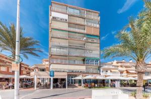 a tall building with a palm tree in front of it at Apartamento en 1ª línea de playa con parking privado in El Campello