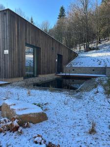 a wooden house in a field with snow on the ground at Apartmány Hraničná s privátním wellness in Bedřichov