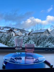 Ein Teller und zwei Gläser auf einem Tisch mit einem Fenster in der Unterkunft Les Couleurs du Lac in Gérardmer