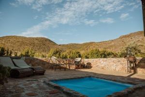 Un patio trasero con piscina y una mesa y sillas. en Wild Olive Cottage, en Graaff-Reinet