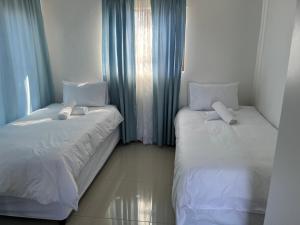 two beds in a room with blue curtains at SNE Travellers in Faure