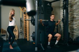 a man and woman in a gym performing squats at Peaks Place Apartments & SPA in Laax
