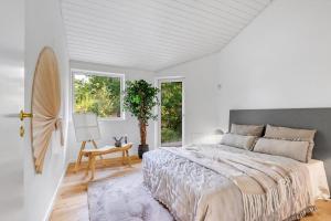 a white bedroom with a large bed and a chair at Arkitekttegnet Sommerhus Tæt På Vandet in Marielyst