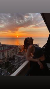 Eine Frau steht auf einem Balkon mit Blick auf den Sonnenuntergang. in der Unterkunft Orbi new batumi in Batumi