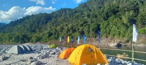 a group of tents on a rocky beach next to a river at Sunset Riverside Camping in Dawki