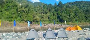 a group of tents on a rocky shore with trees at Sunset Riverside Camping in Dawki