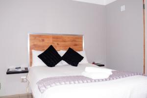Un dormitorio con una cama blanca con almohadas negras. en @Home BnB, en Maseru