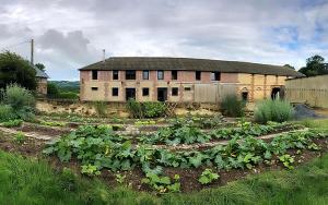 Un edificio antiguo con un huerto de verduras delante. en Hameau Fleuri, en Pierrefitte-en-Auge