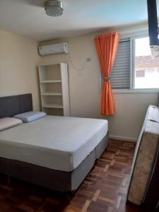 ein Schlafzimmer mit einem Bett und einem Fenster mit einem orangen Vorhang in der Unterkunft Sobrado aconchegante com Piscina Ar Condicionado 3 quartos a 150 metros do mar no Brejatuba in Guaratuba