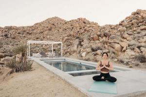 a woman sitting in a yoga pose next to a pool at Bolder House By The Cohost Company in Joshua Tree