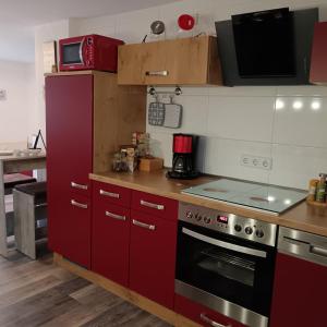 La cuisine est équipée de placards rouges et d'un four avec plaques de cuisson. dans l'établissement Haus Maisonette am Harz, à Niedersachswerfen