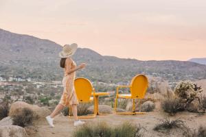 a woman in a hat walking past two chairs at Mandarin Escape By The Cohost Company in Yucca Valley
