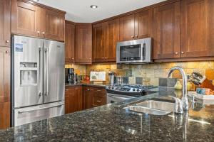 a kitchen with wooden cabinets and a stainless steel refrigerator at 2BR Modern Luxe Condo with Hot Tub and Views in Canmore +55 photos