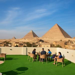 een groep mensen die aan tafels op gras zitten met piramides op de achtergrond bij The Tree Pyramids Inn in Caïro