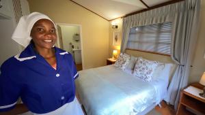 Eine Frau steht in einem Zimmer mit einem Bett in der Unterkunft Cabin & Cottage Kaapsehoop in Kaapsehoop