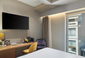 a hotel room with a bed and a desk and a tv at NYX Hotel Thessaloniki in Thessaloniki