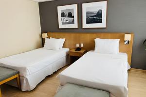 two beds in a hotel room with white sheets at Mediterrâneo Flat in Rio de Janeiro