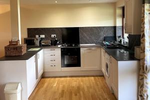 a kitchen with white cabinets and black counter tops at Woodside Cottages - Beech cottage - Self-catering in Fletching