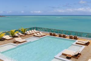 a swimming pool with lounge chairs and the ocean at Sais Beach Living Hotel in Maceió
