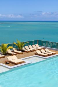 a swimming pool with lounge chairs and the ocean at Sais Beach Living Hotel in Maceió