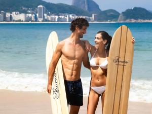 a man and a woman standing on the beach with surfboards at Fairmont Rio de Janeiro Copacabana in Rio de Janeiro