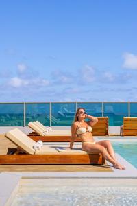 a woman in a bikini sitting on a bench next to a pool at Sais Beach Living Hotel in Maceió