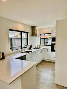 uma grande cozinha com armários brancos e janelas em Modern Costal Escape-with Spa em Papamoa