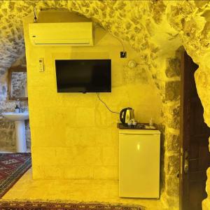 a room with a yellow wall with a tv on it at Kasr-ı Han Konağı Otel in Mardin